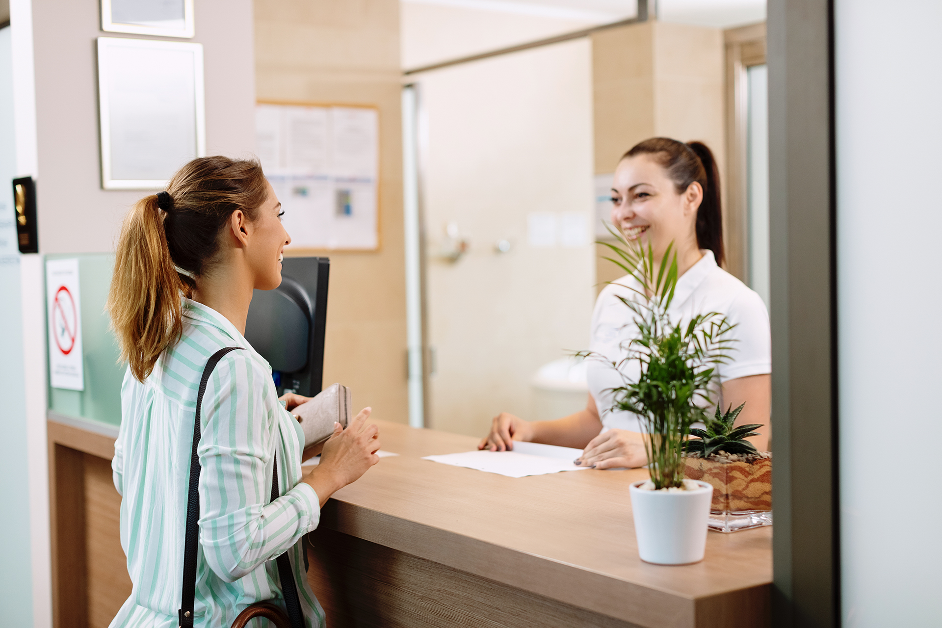 Young happy woman checking in health spa and communicating with a receptionist.